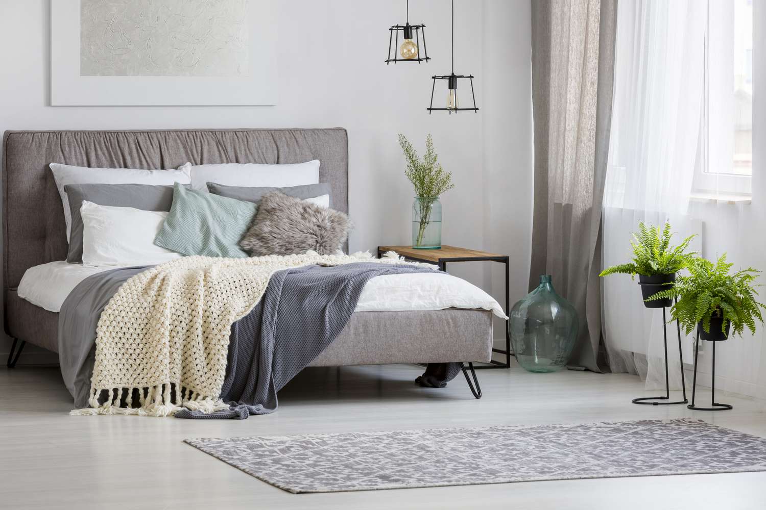 Grey, modern bedroom interior with king-size bed decorated with cushions and blankets