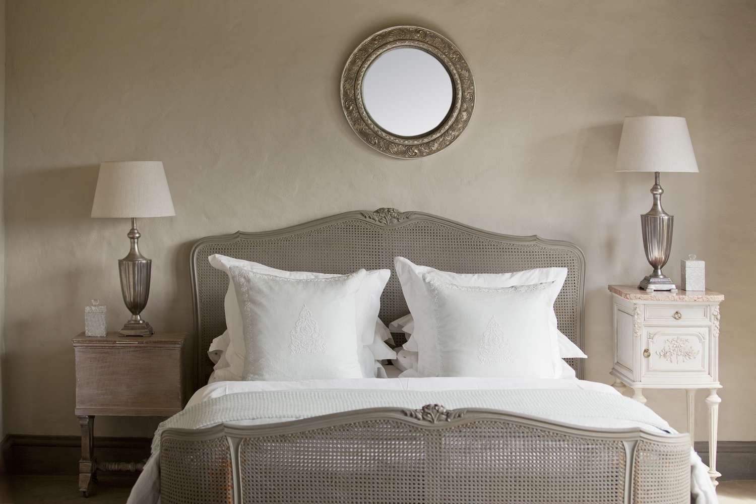 Gray bedroom with bed, two end tables, two lamps, and a mirror over the bed.